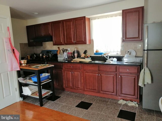 kitchen with range hood, backsplash, sink, and stainless steel fridge