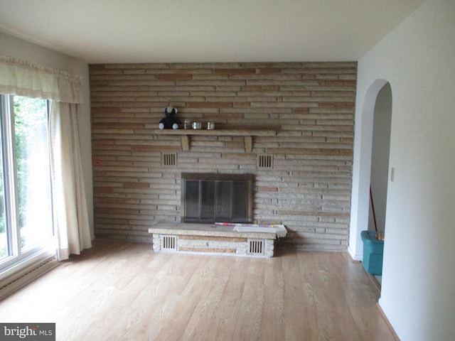 unfurnished living room featuring a brick fireplace, hardwood / wood-style flooring, and a wealth of natural light