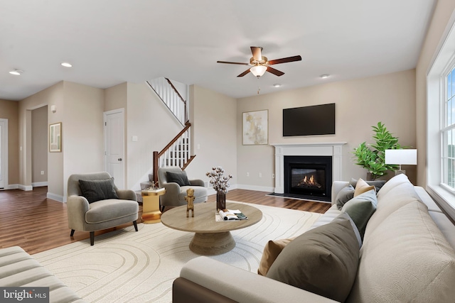 living area featuring ceiling fan, baseboards, wood finished floors, and stairs