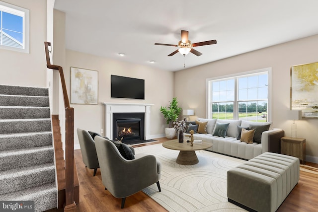 living room with ceiling fan, a fireplace with flush hearth, wood finished floors, and stairs