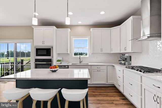 kitchen featuring a sink, appliances with stainless steel finishes, white cabinetry, wall chimney exhaust hood, and tasteful backsplash