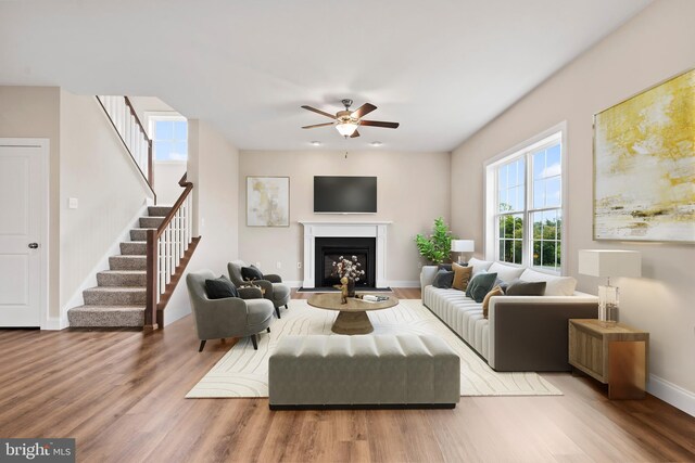 living room featuring wood finished floors, stairway, a fireplace, baseboards, and ceiling fan