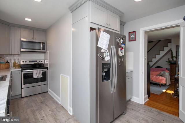 kitchen featuring gray cabinets, stainless steel appliances, backsplash, and light hardwood / wood-style flooring