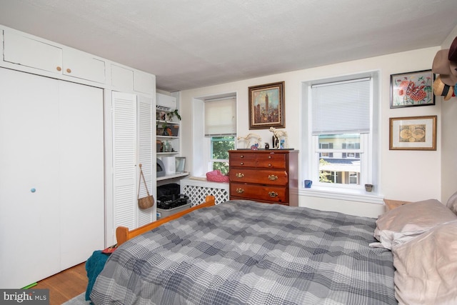 bedroom with multiple windows, a textured ceiling, a wall unit AC, and hardwood / wood-style flooring