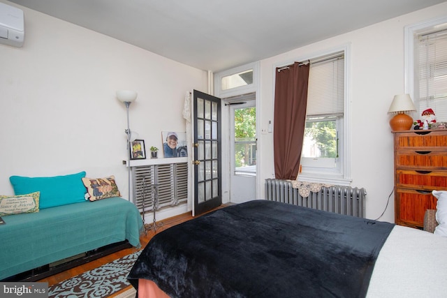 bedroom featuring an AC wall unit, radiator heating unit, and hardwood / wood-style flooring