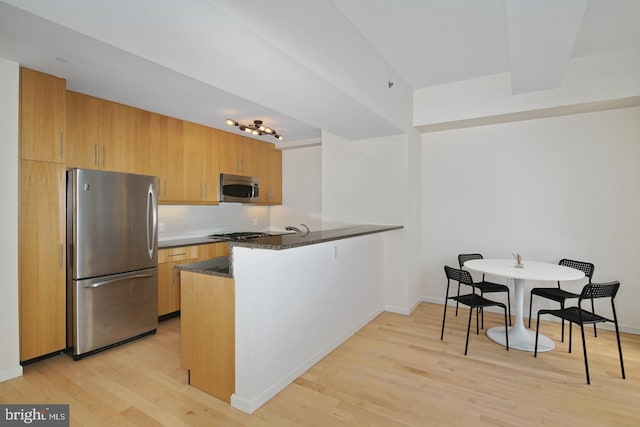 kitchen with light hardwood / wood-style floors, kitchen peninsula, dark stone countertops, and stainless steel appliances