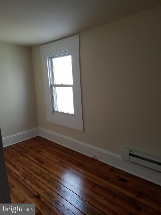 empty room featuring dark hardwood / wood-style floors and a baseboard heating unit