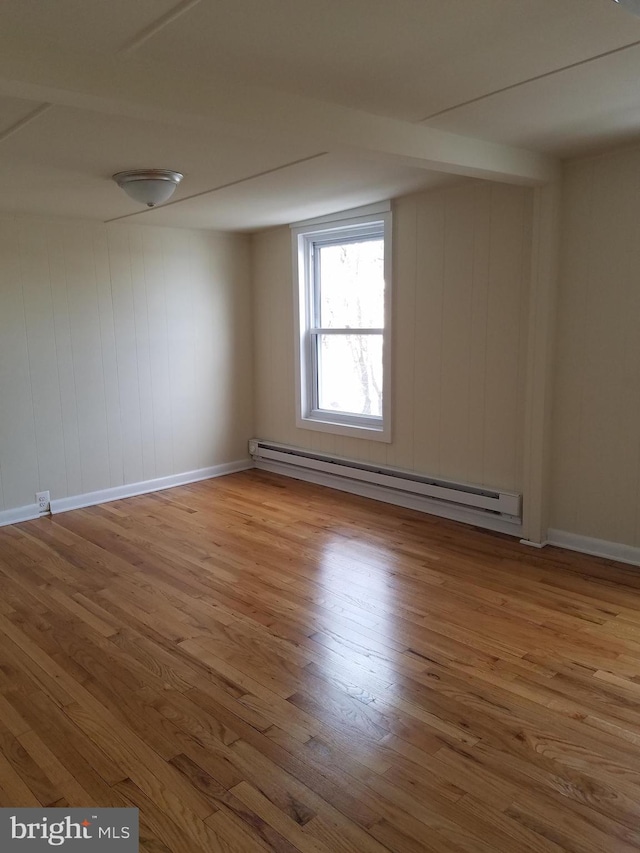 empty room with wood-type flooring, a baseboard radiator, and wood walls