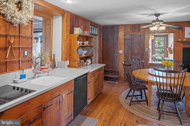 kitchen with light hardwood / wood-style floors, black appliances, sink, and wooden walls