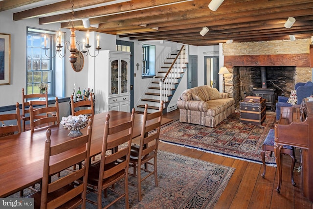 dining space with a wood stove, wood-type flooring, and beamed ceiling