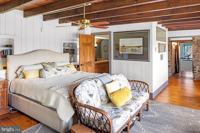 bedroom featuring beam ceiling, wood-type flooring, wooden walls, and ceiling fan