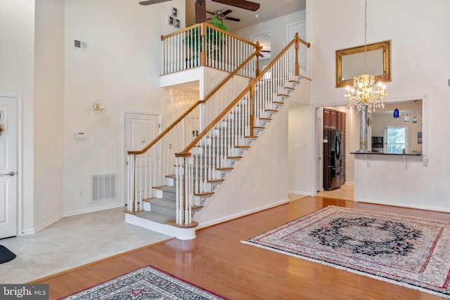 entryway with ceiling fan with notable chandelier, a high ceiling, and light wood-type flooring