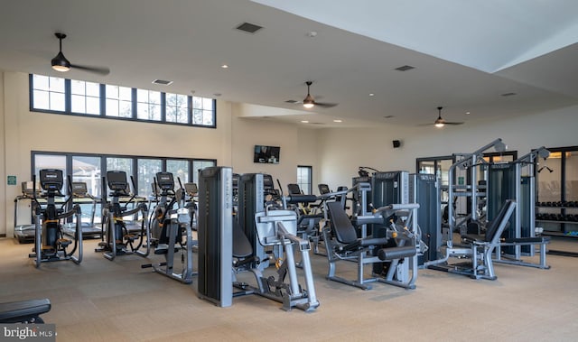 exercise room with ceiling fan, light colored carpet, and a towering ceiling