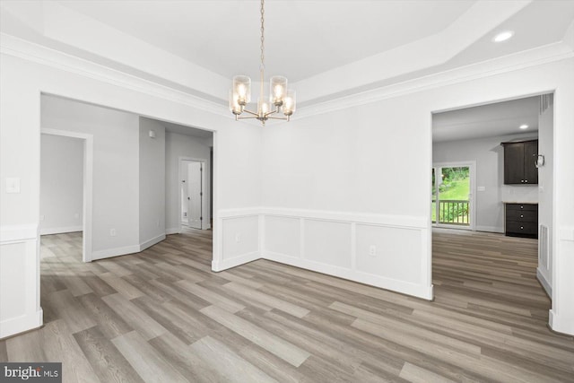 empty room with a raised ceiling, a chandelier, light hardwood / wood-style floors, and crown molding