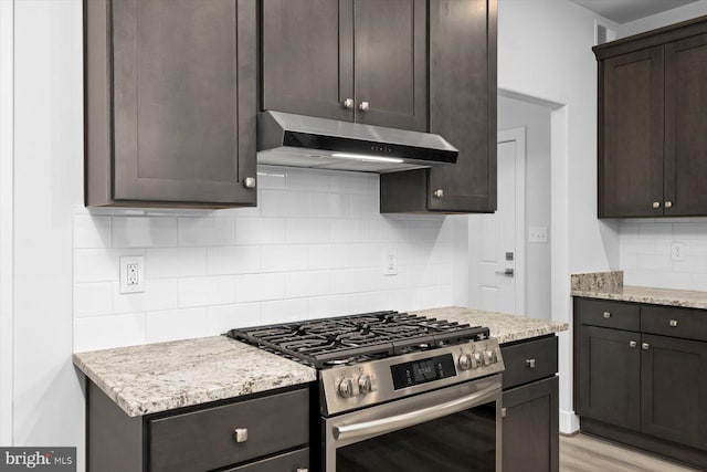 kitchen with dark brown cabinets, high end stainless steel range oven, light hardwood / wood-style floors, light stone counters, and decorative backsplash