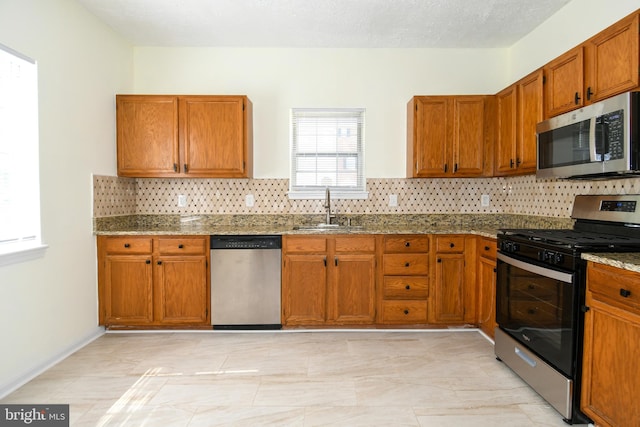 kitchen featuring a textured ceiling, sink, decorative backsplash, appliances with stainless steel finishes, and light stone countertops