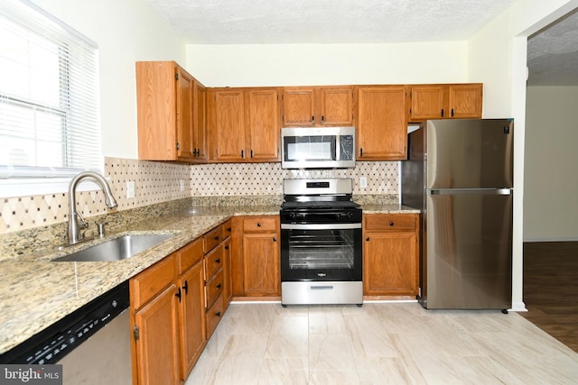 kitchen with decorative backsplash, light stone counters, appliances with stainless steel finishes, and sink