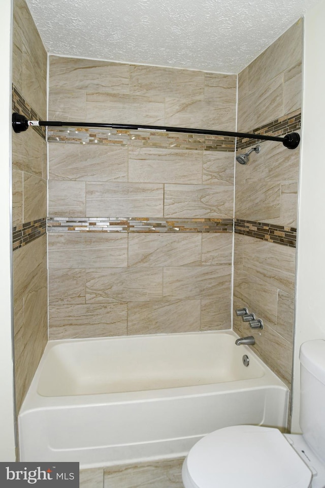 bathroom featuring a textured ceiling, tiled shower / bath combo, and toilet