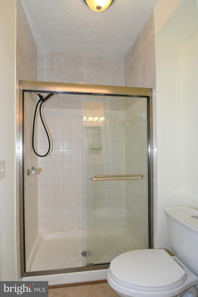 bathroom featuring walk in shower, a textured ceiling, toilet, and tile patterned floors