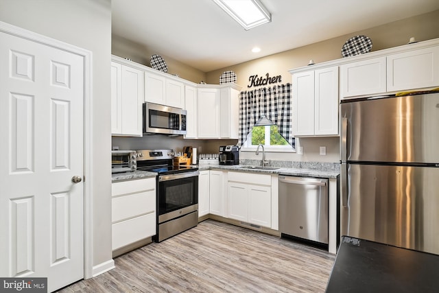 kitchen featuring appliances with stainless steel finishes, white cabinetry, light stone counters, light hardwood / wood-style flooring, and sink