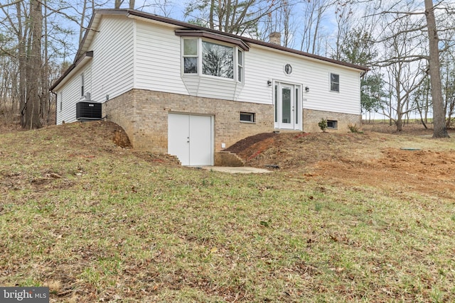 bi-level home featuring brick siding, cooling unit, a front lawn, and a chimney