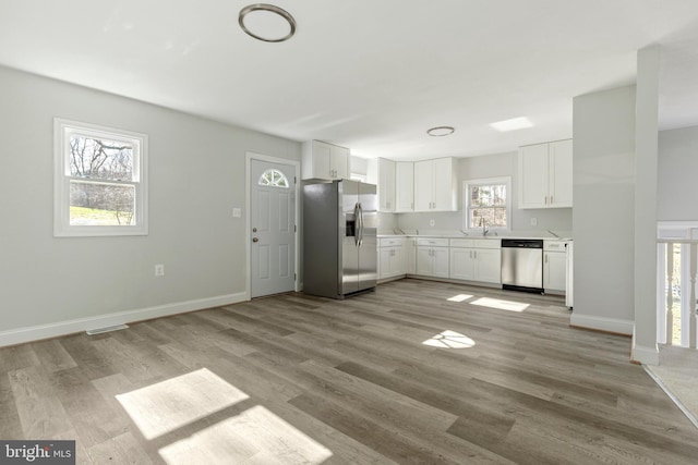 kitchen with light wood finished floors, light countertops, white cabinets, stainless steel appliances, and a sink