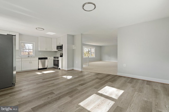 unfurnished living room with a sink, baseboards, light wood-style floors, and a healthy amount of sunlight