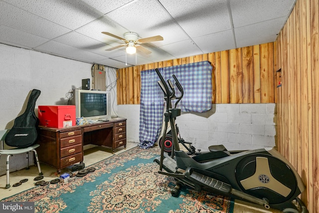 exercise room with a drop ceiling, wooden walls, and ceiling fan