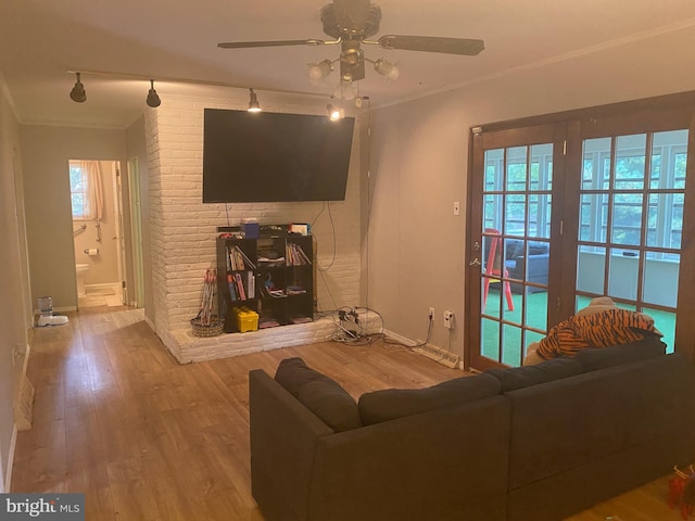 living room featuring ceiling fan, light wood-type flooring, a brick fireplace, and a healthy amount of sunlight