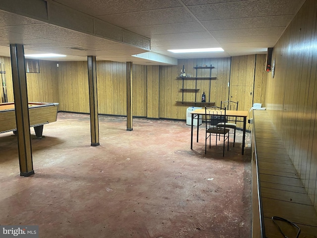 basement featuring a drop ceiling and wooden walls