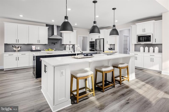 kitchen with white cabinets, hanging light fixtures, wall chimney exhaust hood, stainless steel refrigerator with ice dispenser, and a spacious island