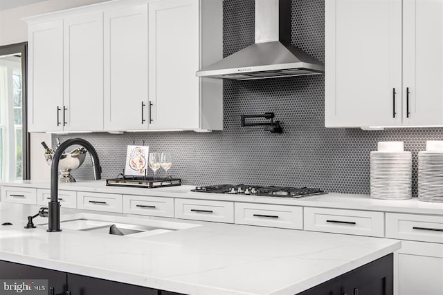 kitchen with sink, stainless steel gas cooktop, wall chimney range hood, white cabinetry, and decorative backsplash