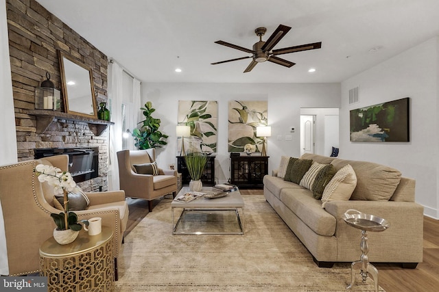 living room featuring ceiling fan, a fireplace, and light wood-type flooring