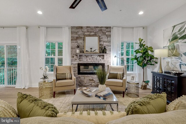 living room featuring a stone fireplace, ceiling fan, and light hardwood / wood-style flooring