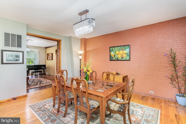 dining room with a notable chandelier, light hardwood / wood-style floors, and brick wall