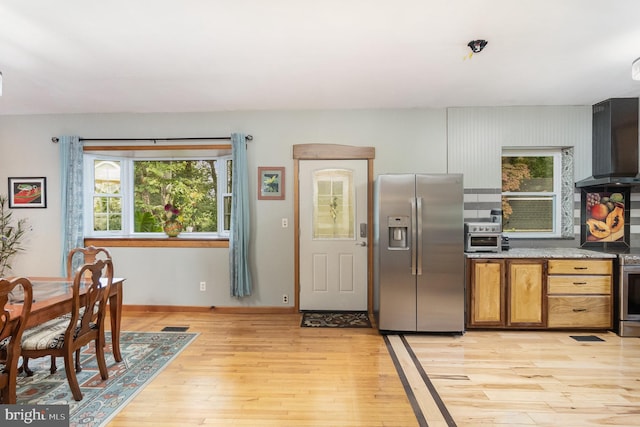 kitchen featuring light wood-type flooring, wall chimney exhaust hood, stainless steel fridge, and plenty of natural light