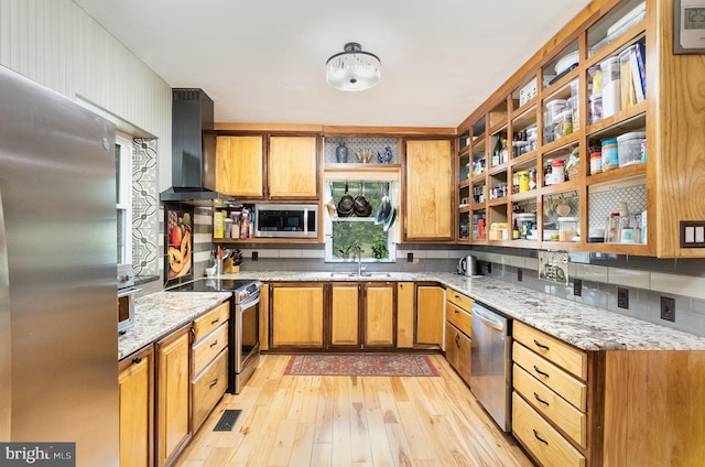 kitchen featuring light stone counters, sink, wall chimney exhaust hood, light hardwood / wood-style flooring, and appliances with stainless steel finishes