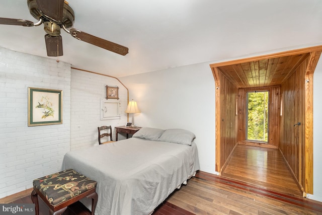 bedroom featuring wooden walls, ceiling fan, brick wall, and hardwood / wood-style floors