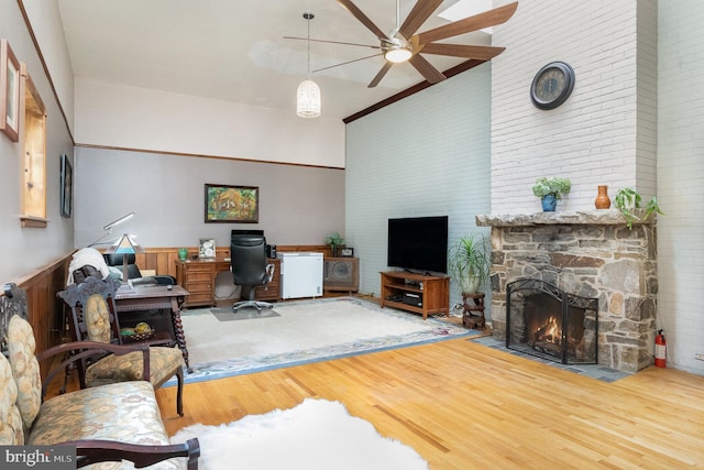 living room featuring hardwood / wood-style flooring, a stone fireplace, ornamental molding, a high ceiling, and ceiling fan