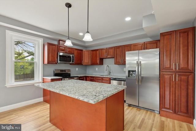 kitchen with appliances with stainless steel finishes, a kitchen island, pendant lighting, light wood-type flooring, and sink