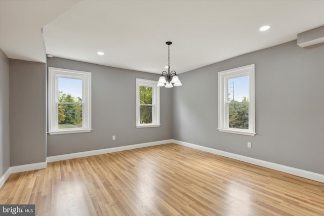 unfurnished room featuring light hardwood / wood-style flooring, a notable chandelier, and a healthy amount of sunlight