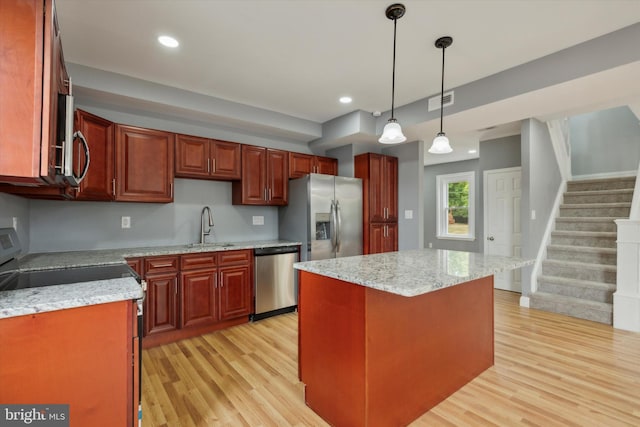 kitchen with pendant lighting, light wood-type flooring, sink, a kitchen island, and stainless steel appliances