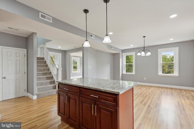 kitchen featuring hanging light fixtures, light stone counters, light wood-type flooring, a center island, and a chandelier