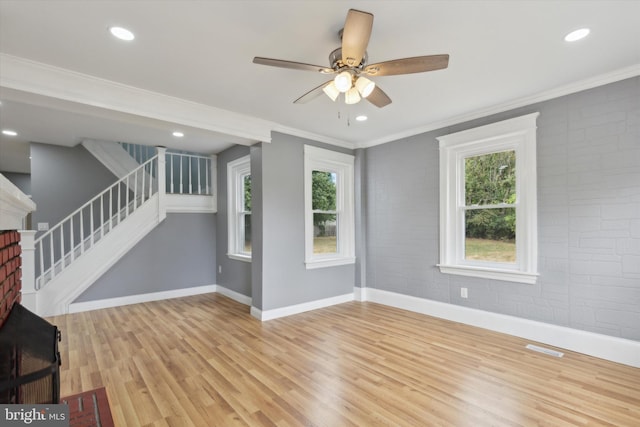 unfurnished living room with light wood-type flooring, ceiling fan, brick wall, and crown molding