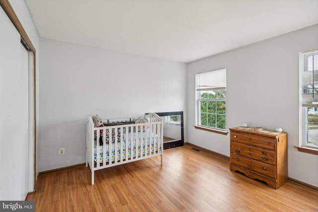 bedroom featuring multiple windows, a crib, a closet, and hardwood / wood-style flooring