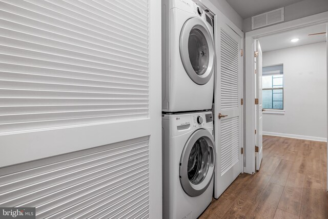 washroom with wood-type flooring and stacked washer / drying machine