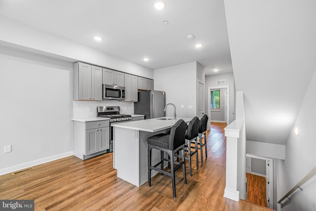 kitchen featuring a breakfast bar area, gray cabinetry, stainless steel appliances, an island with sink, and light hardwood / wood-style floors