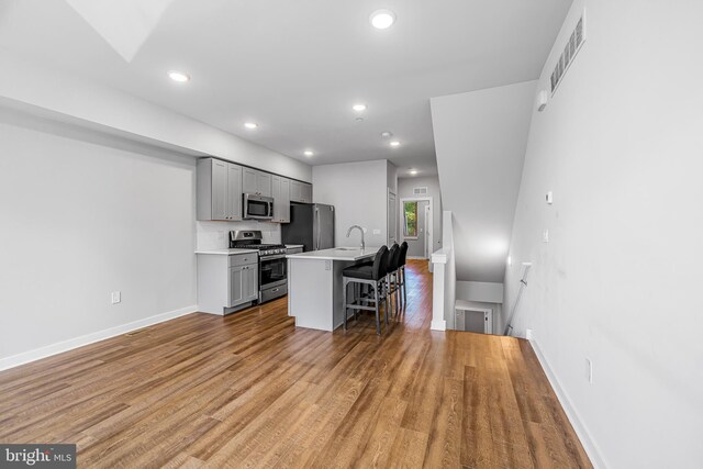 kitchen with stainless steel appliances, a breakfast bar, tasteful backsplash, gray cabinets, and a kitchen island with sink