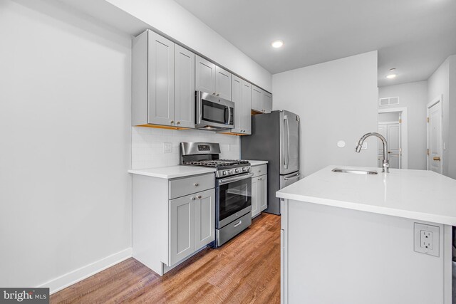 kitchen with stainless steel appliances, light hardwood / wood-style floors, tasteful backsplash, and sink