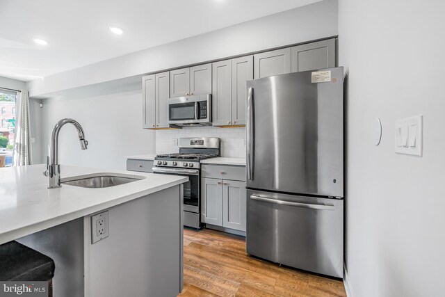 kitchen with stainless steel appliances, light wood-type flooring, backsplash, gray cabinetry, and sink